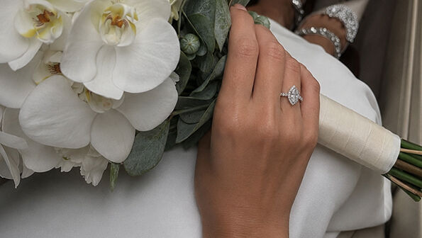 Close-up of a hand holding a gold engagement ring with a round diamond halo setting