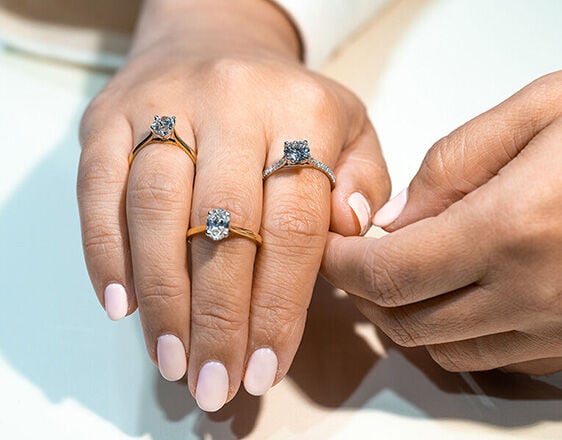Hand wearing a selection of oval and round diamond engagement rings in yellow gold and white gold.