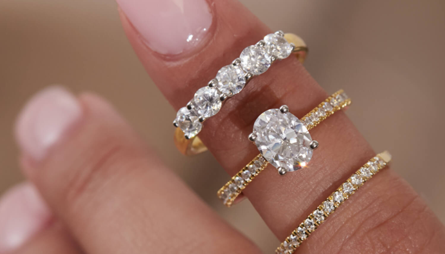 Close-up of an oval-cut diamond engagement ring with pavé band, styled with gold diamond eternity bands.