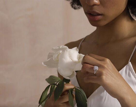 Woman wearing a square halo diamond engagement ring while holding a white flower.