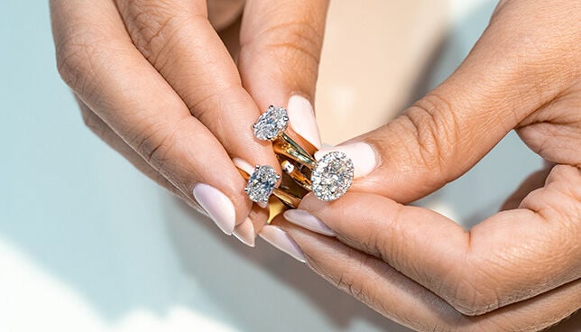 Hands holding three gold solitaire engagement rings with diamonds