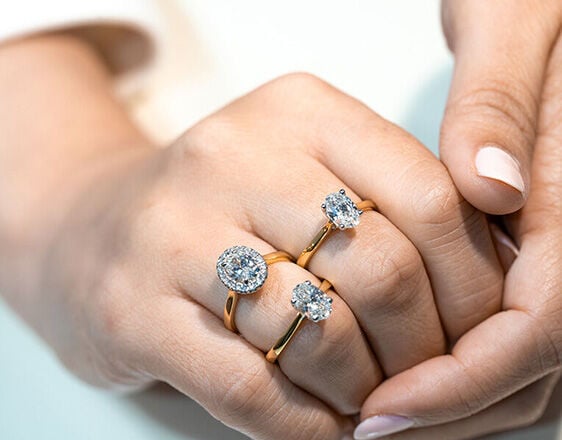 Close-up of hands showcasing halo and round solitaire diamond engagement rings in yellow gold.